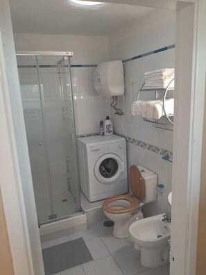 Ein kleines Badezimmer mit Duschkabine, Waschmaschine, Toilette und Bidet.