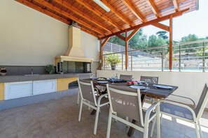 An outdoor kitchen with a grill, dining table, and chairs.