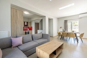 Een moderne woonkamer met een bank, een houten salontafel en een eethoek met stoelen en een tafel.