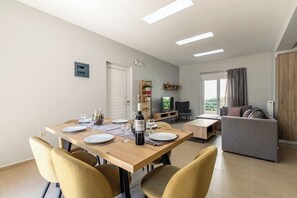 A dining area with a wooden table set for four, a sofa, and a TV in the background.