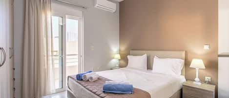 Una habitación de hotel con cama, mesitas de noche, lámpara, ventana con cortinas y aire acondicionado.