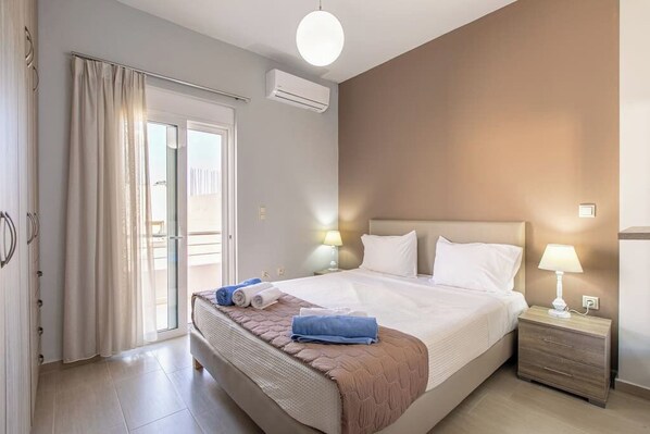 A hotel room with a bed, bedside tables, a lamp, a window with curtains, and an air conditioning unit.