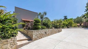 A spacious outdoor area with a stone wall, a paved walkway, and various plants. - Neaira Villas - Villa no2 with private pool (Platanias)
