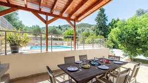 Un espace repas extérieur avec vue sur la piscine, agrémenté d’une pergola en bois et d’une table dressée pour quatre personnes.