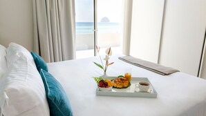 Habitación de hotel con cama, bandeja de desayuno y vista a la playa.