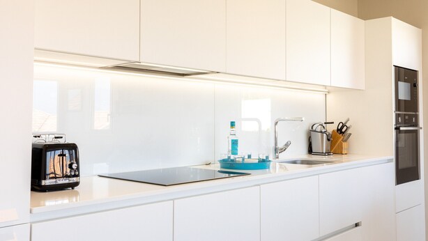 Una cocina moderna con armarios blancos, horno empotrado y tostadora.