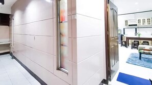 Un passadís d'hotel modern amb un gran finestral, una zona de menjador amb una catifa blava, i una cuina al fons.