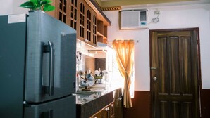Cuina amb nevera, armaris de fusta, finestra amb cortines i una porta.