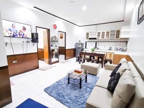 Una sala de estar moderna con un sofá, una mesa de centro y un televisor. Hay una zona de cocina con armarios y una mesa de comedor.