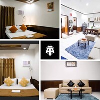 Habitación de hotel con cama, mesita de noche y ventana con cortinas. Incluye baño con ducha, inodoro y lavamanos. El piso es de madera y la pared es blanca.