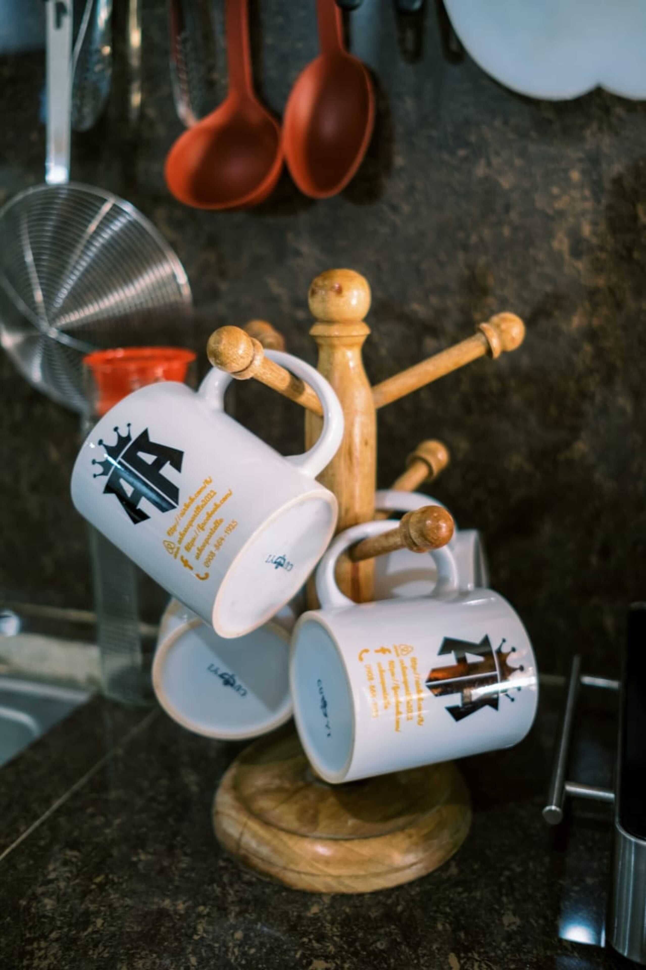 Una encimera de cocina con un estante de madera para especias que contiene varias tazas blancas con diseños negros y dorados.