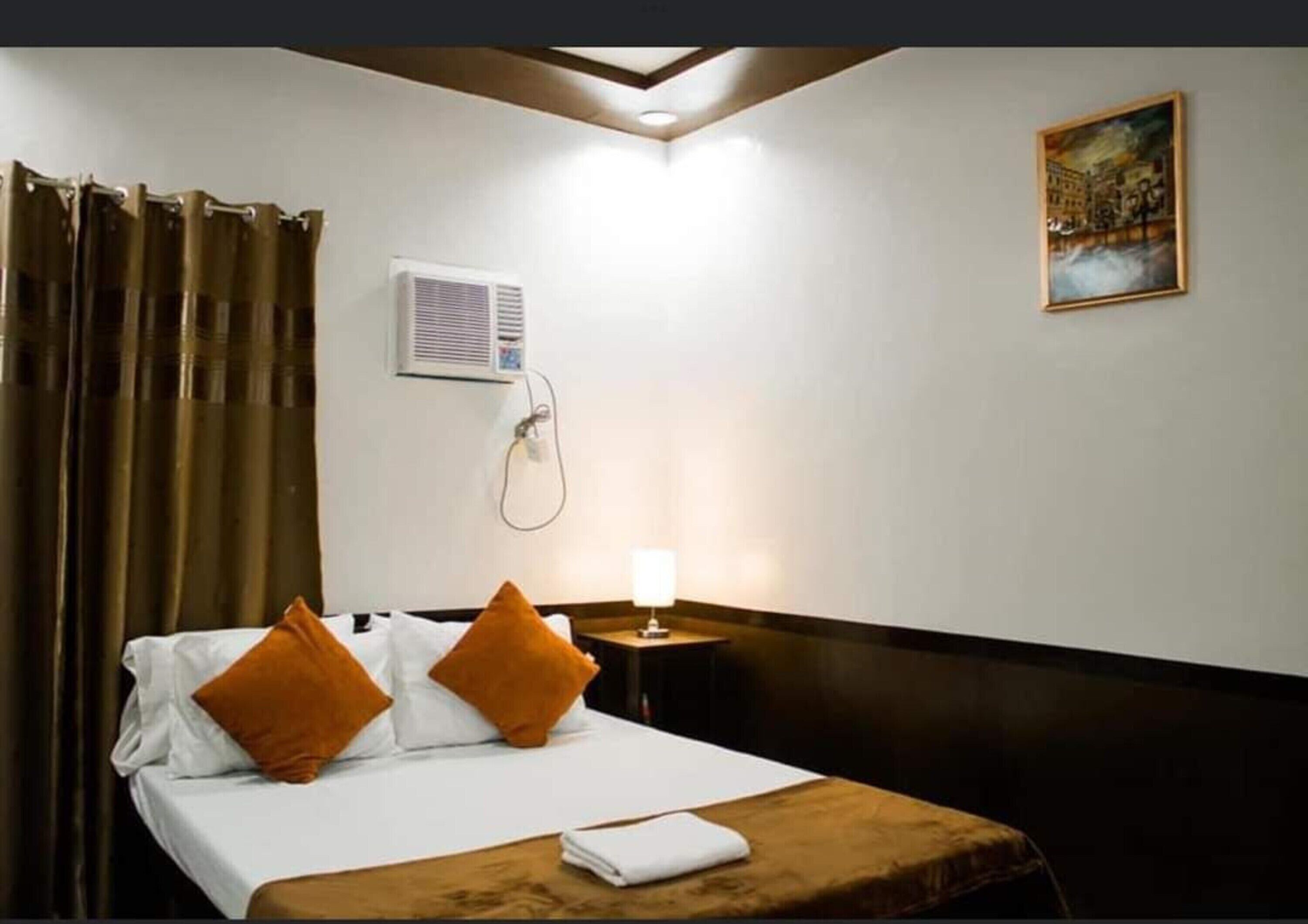 A hotel room with a bed, a nightstand, a lamp, a painting on the wall, and a window with curtains.