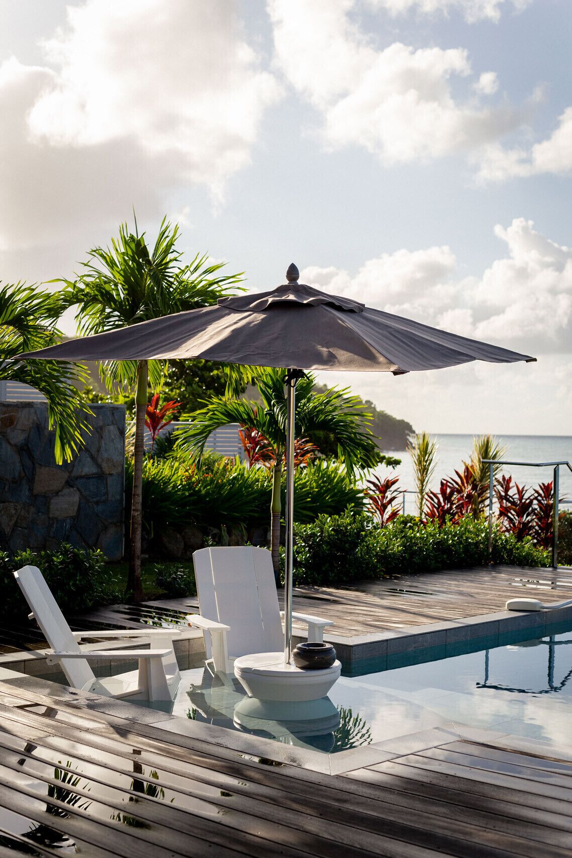 Un área junto a la piscina con sillones de descanso, un cuenco decorativo y una sombrilla.