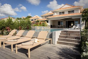 Un espace aménagé au bord de la piscine, avec des chaises longues, une piscine et un bâtiment doté d’un toit en tuiles.