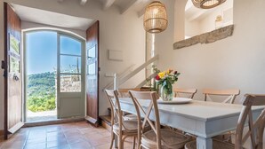 A dining area with a white table and wicker chairs, a vase with flowers, and a view of greenery through a glass door.