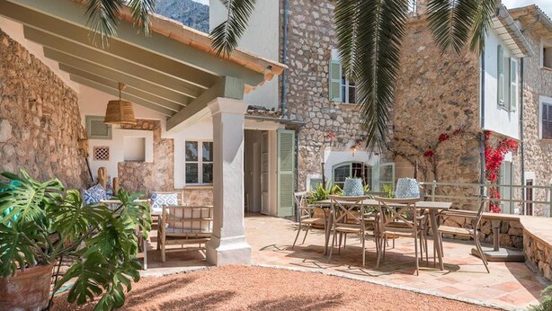 A stone house with a patio area featuring a table and chairs, surrounded by potted plants and a stone wall.