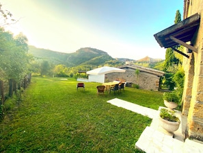 Un'area verde con un edificio bianco, un muro in pietra e una vista sulle colline sullo sfondo.
