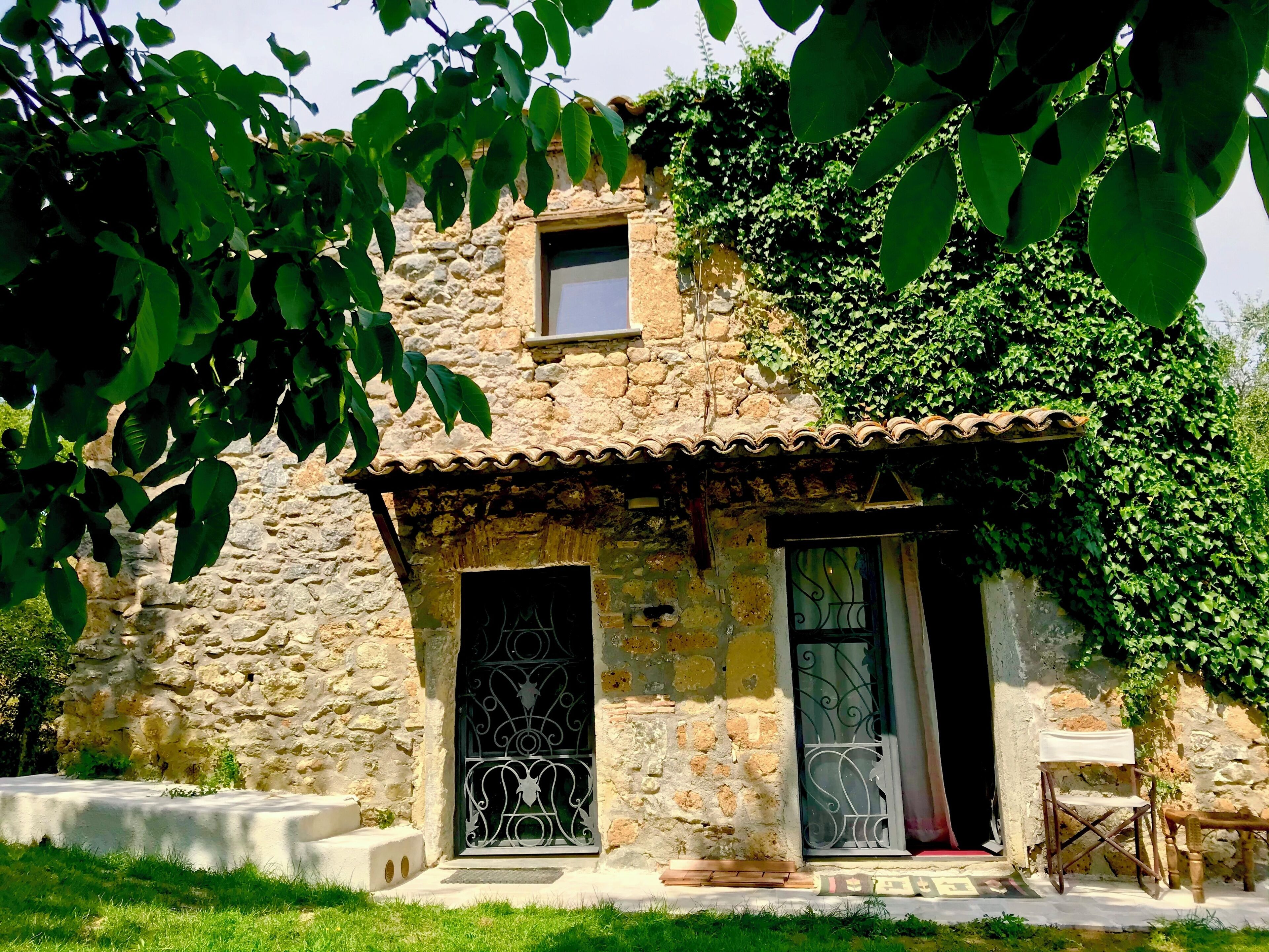 Ein Steinhaus mit einem kleinen Fenster und einer Tür, umgeben von viel Grün.