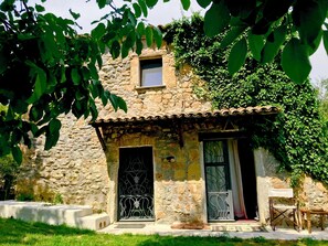 Un bâtiment en pierre avec une petite fenêtre et une porte, entouré de verdure.