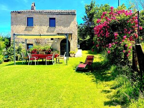 Un bâtiment en pierre doté d’un patio couvert, d’une table avec des chaises et d’un jardin fleuri.