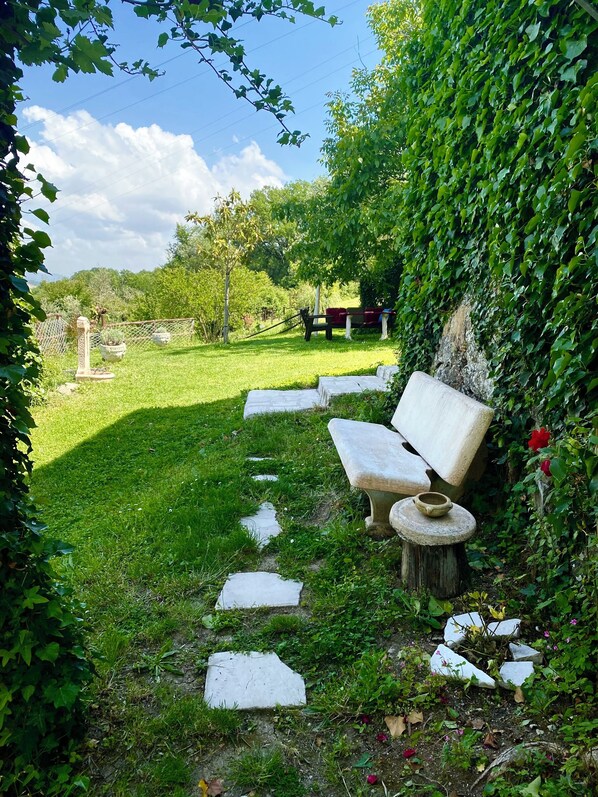 A garden pathway with stepping stones leading to a bench and a table, surrounded by greenery and a fence.