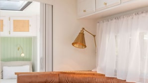 Ein gemütlicher Sitzbereich mit einer braunen Ledbank, einem Holztisch mit einer weißen Kerze und einer goldfarbenen Lampe.