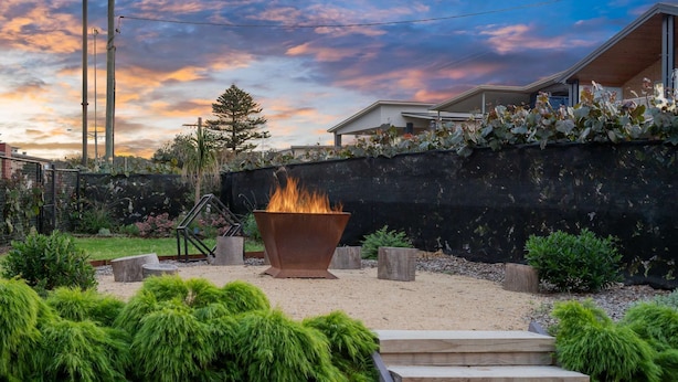 Ein Garten mit Feuerstelle, einer Holzterrasse und einem Haus im Hintergrund.