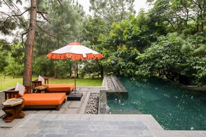 A poolside area with a stone bench, a wooden table, and an umbrella. - Pemako Punakha (Punakha)