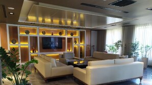 A modern living room with a large flat-screen TV, beige sofas, and a wooden floor. - Hotel Bukhara (Bukhara)