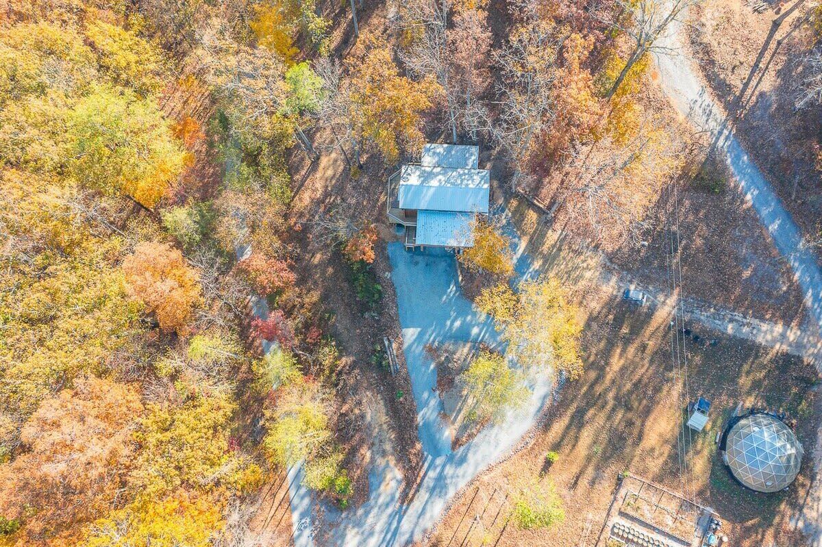 An aerial view of a house surrounded by autumn foliage, with a visible road and a spherical structure nearby.