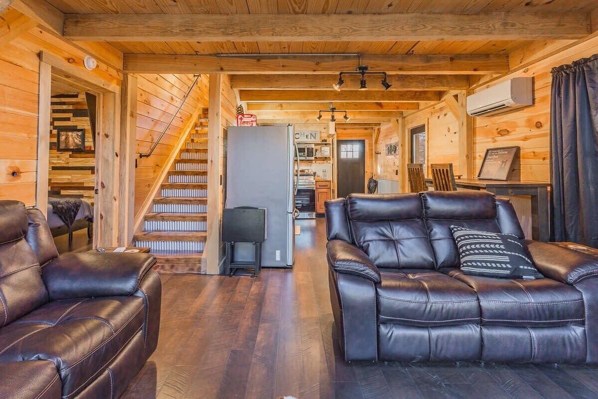 Un intérieur chaleureux de chalet en bois, avec une cheminée, des canapés en cuir, un coin repas et une cuisine.