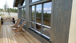A wooden deck with two lounge chairs and a picnic table, overlooking a beach. - New mountain cabin with panoramic view, sauna, ski-in -ski-out (Innlandet)