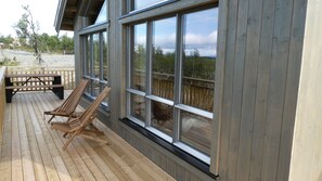 Una terraza de madera con dos sillones de descanso y una mesa de picnic, con vistas a una playa.