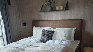 A bed with a wooden headboard, a bedside table, and a small wooden stool. - New mountain cabin with panoramic view, sauna, ski-in -ski-out (Innlandet)
