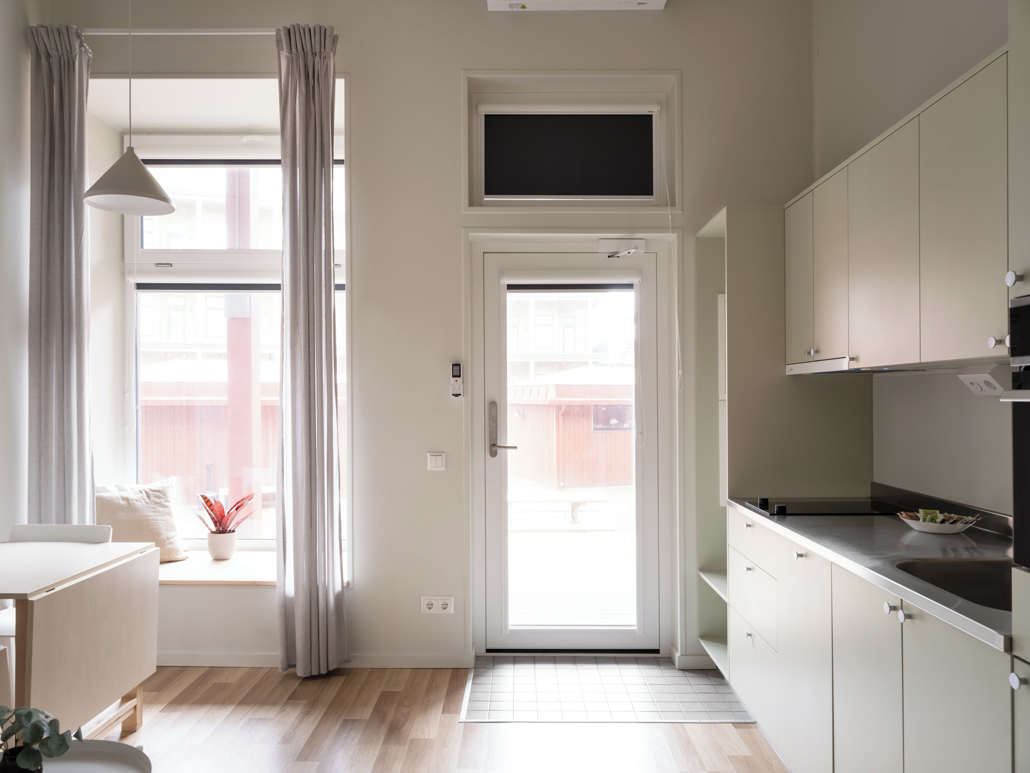 A modern kitchen with white cabinets, a built-in oven, and a window overlooking the street.