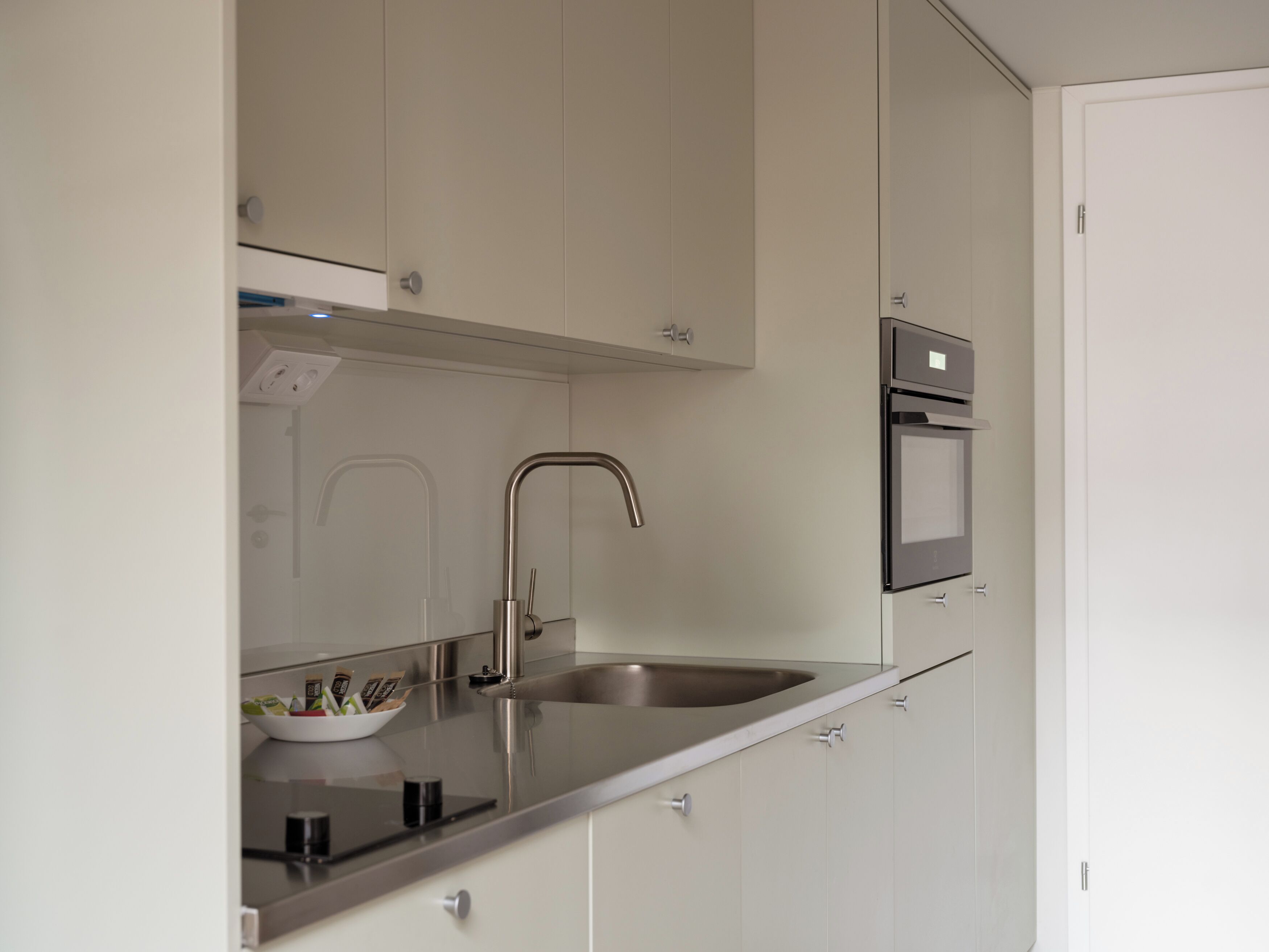A modern kitchen with a stainless steel sink, a built-in oven, and white cabinetry.
