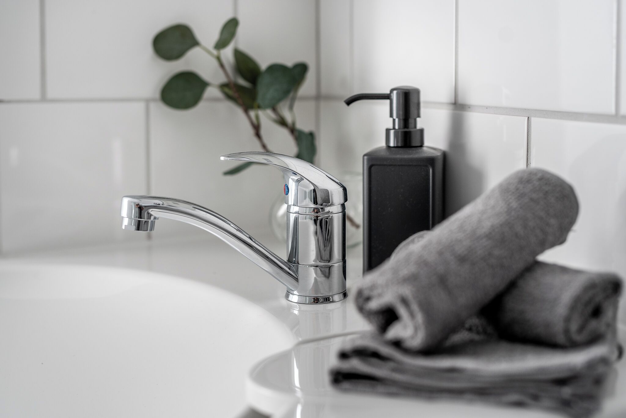 Un baño moderno con un grifo cromado, un dispensador de jabón negro y toallas ordenadamente dobladas sobre el lavamanos.
