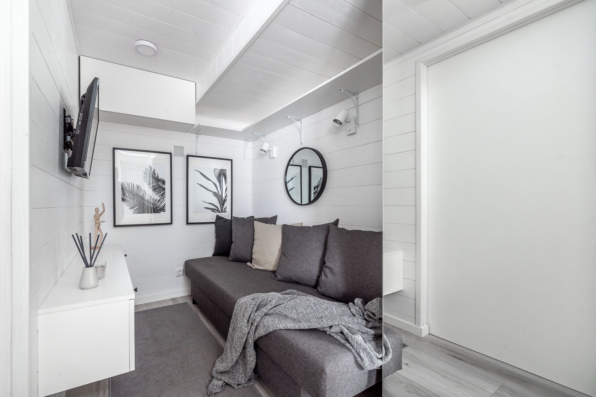 Une chambre à coucher moderne et minimaliste, avec un canapé gris, une table de chevet blanche et un grand miroir.