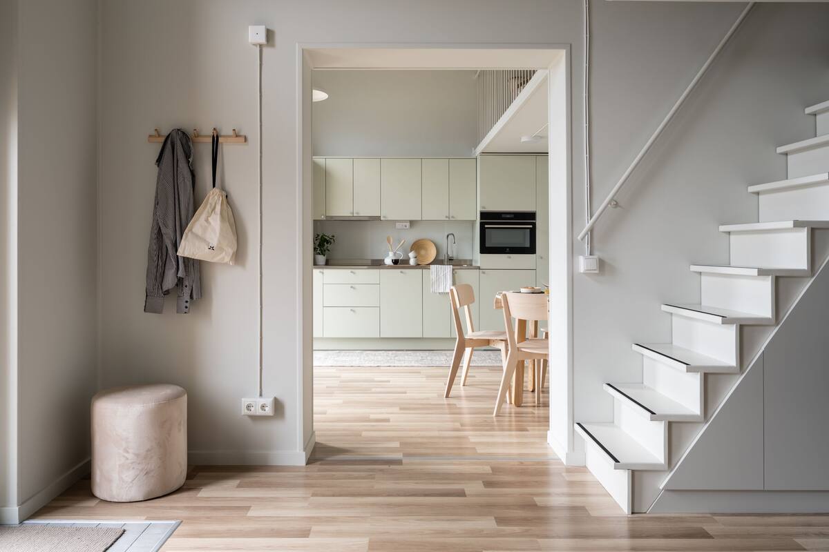 Una cocina moderna con armarios blancos, un comedor con mesa y sillas, y una escalera con escalones blancos.