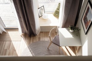 A modern room with a wooden floor, a white desk, a chair, a small potted plant, and a window with curtains.