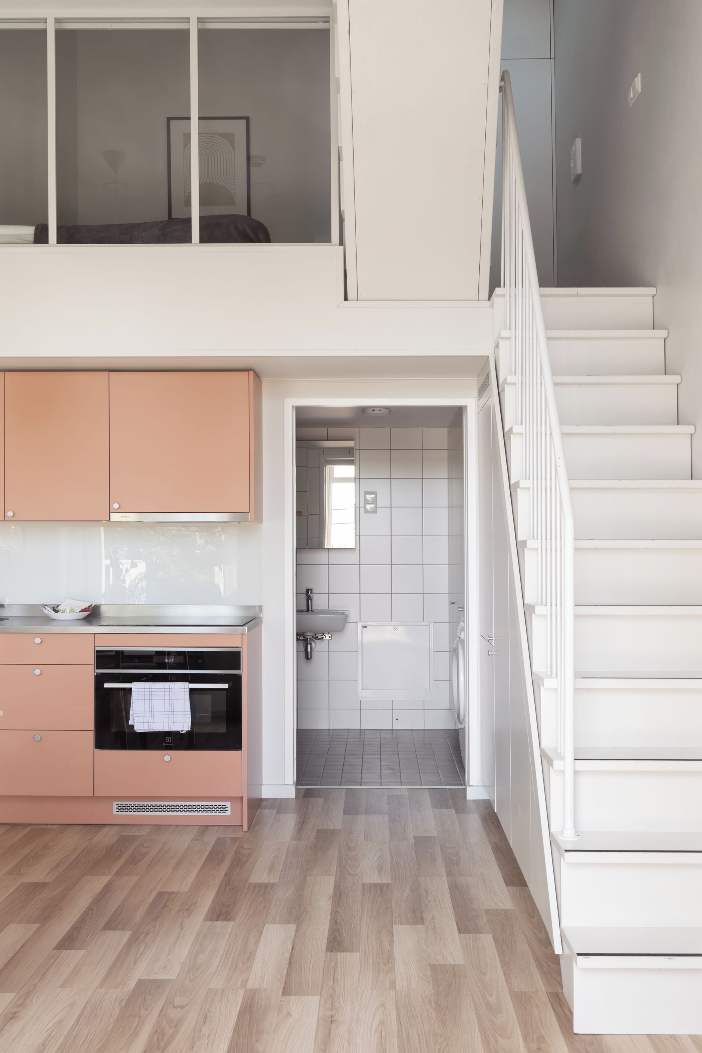 Eine moderne Küche mit Arbeitsplatte und Schränken, einer Treppe und Blick ins Badezimmer.