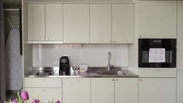 Una cocina moderna con gabinetes blancos, cafetera, lavamanos y refrigerador negro.