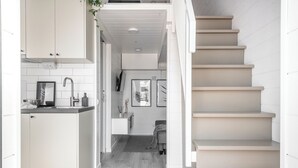A modern kitchen with white cabinetry, a grey countertop, and a staircase leading to an upper level. - Waterfront Cabins Studio Apartments (Gothenburg)