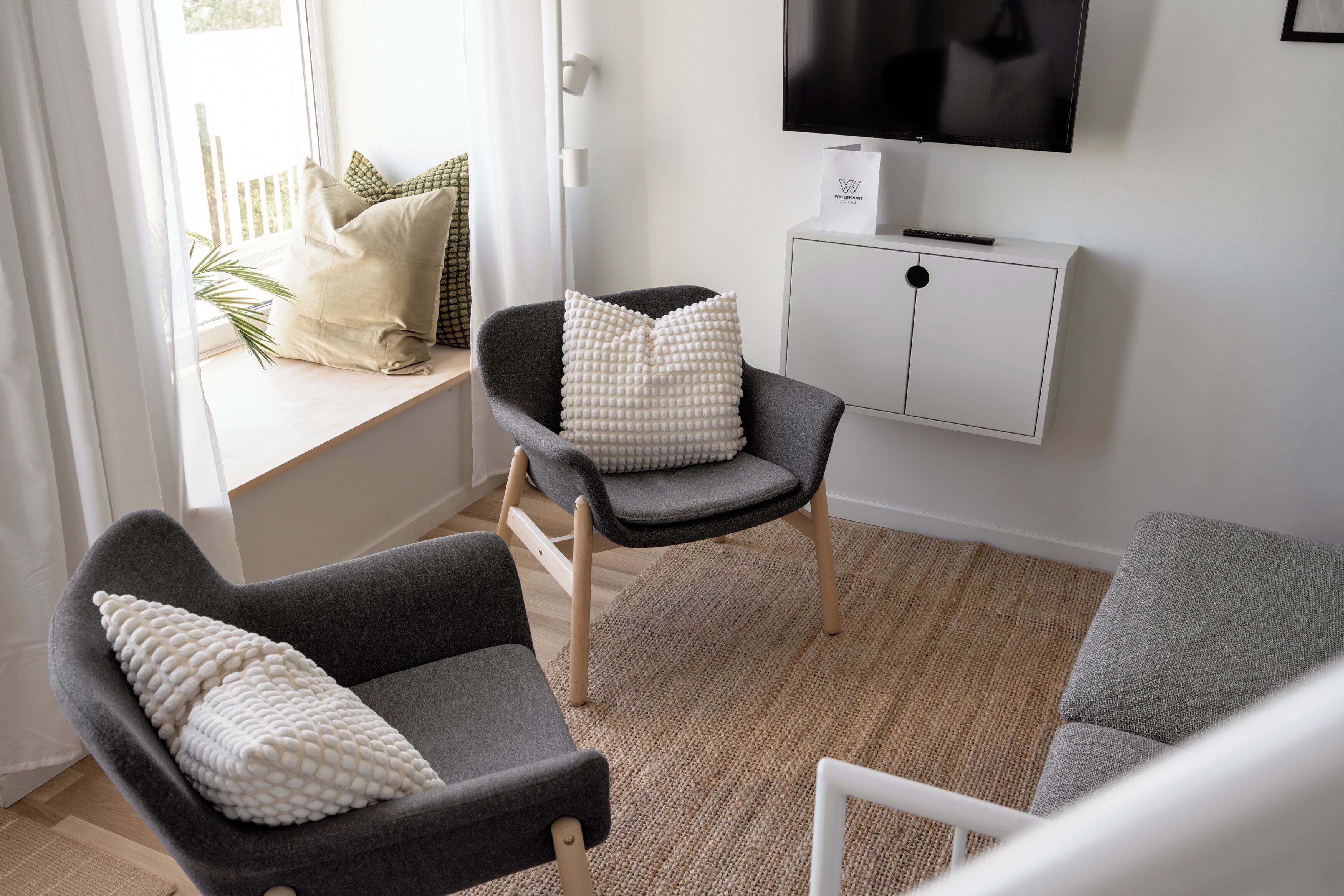 Una sala moderna con un sofá gris, un sillón a juego y una pequeña mesa. Un mueble blanco con un televisor encima está apoyado contra la pared.