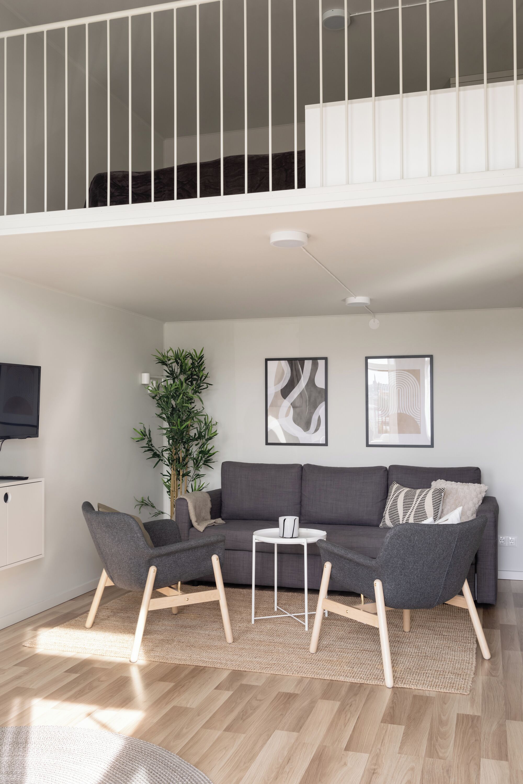 A modern living room with a grey sofa, two armchairs, a small white table, and a large potted plant.