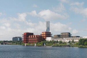 A waterfront view with modern buildings, including a tall skyscraper, and sailboats on the water.