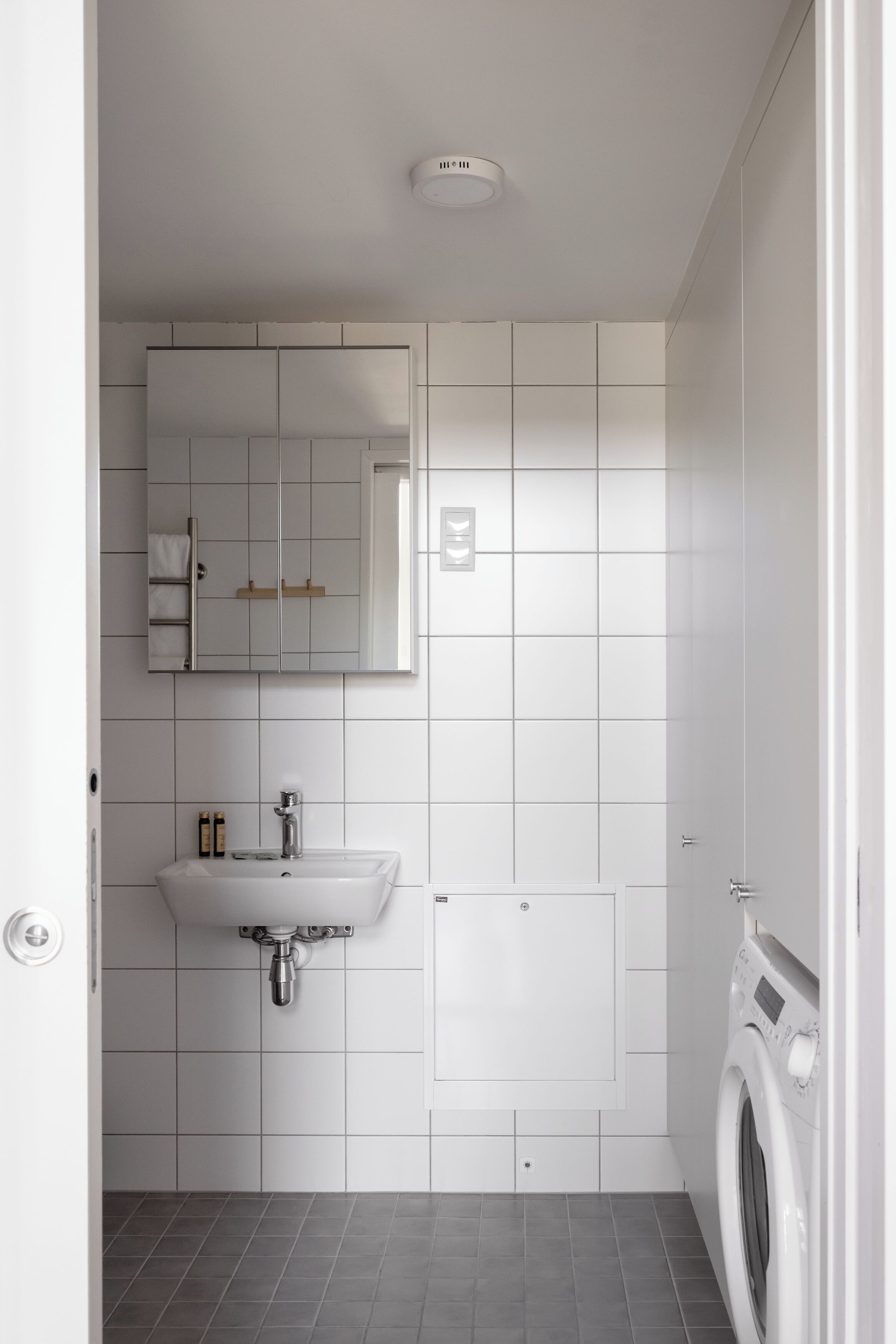 A modern bathroom with a white sink, mirror, and a built-in washing machine.
