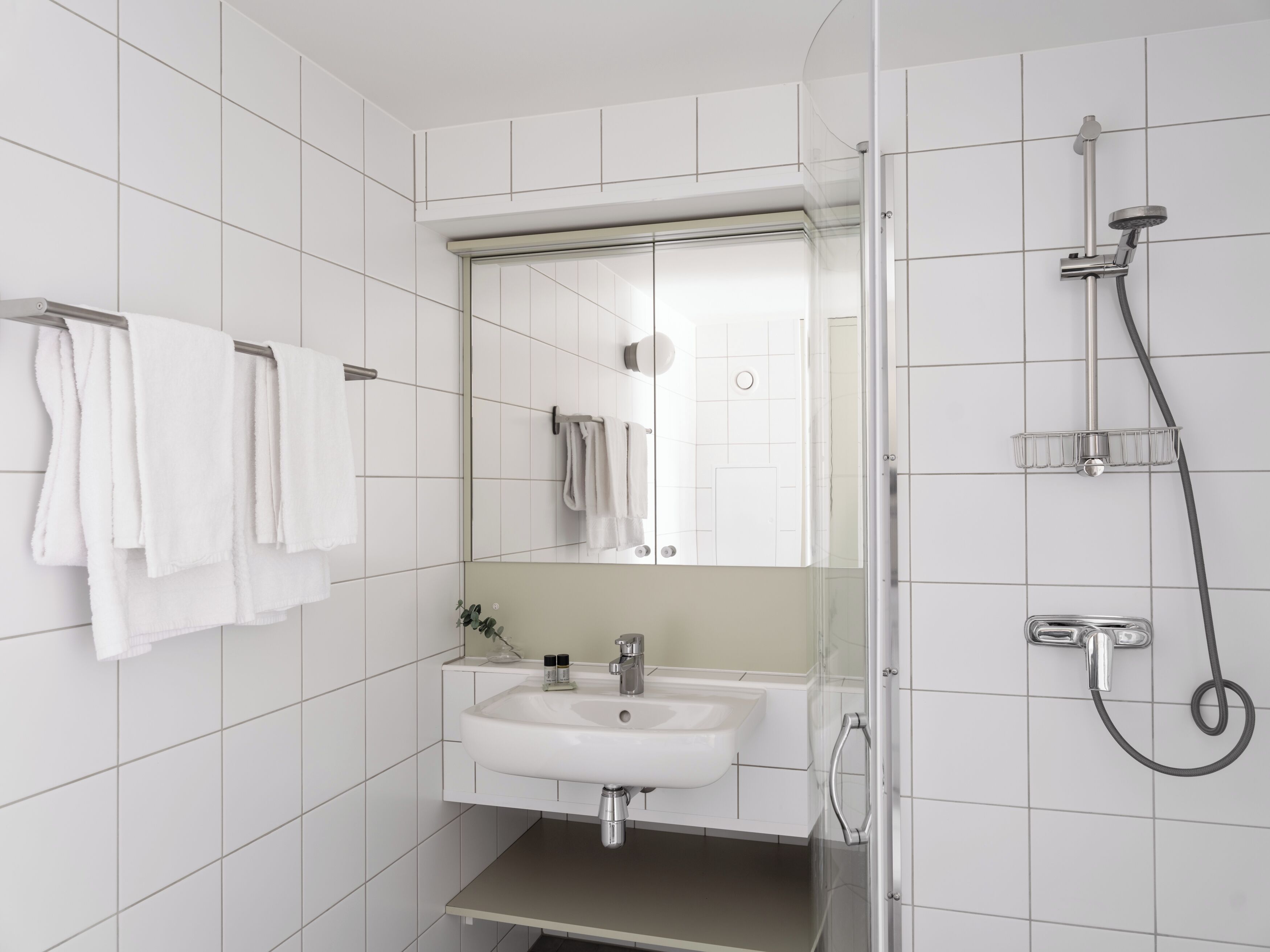 Un baño moderno con lavamanos, espejo y ducha blancos.