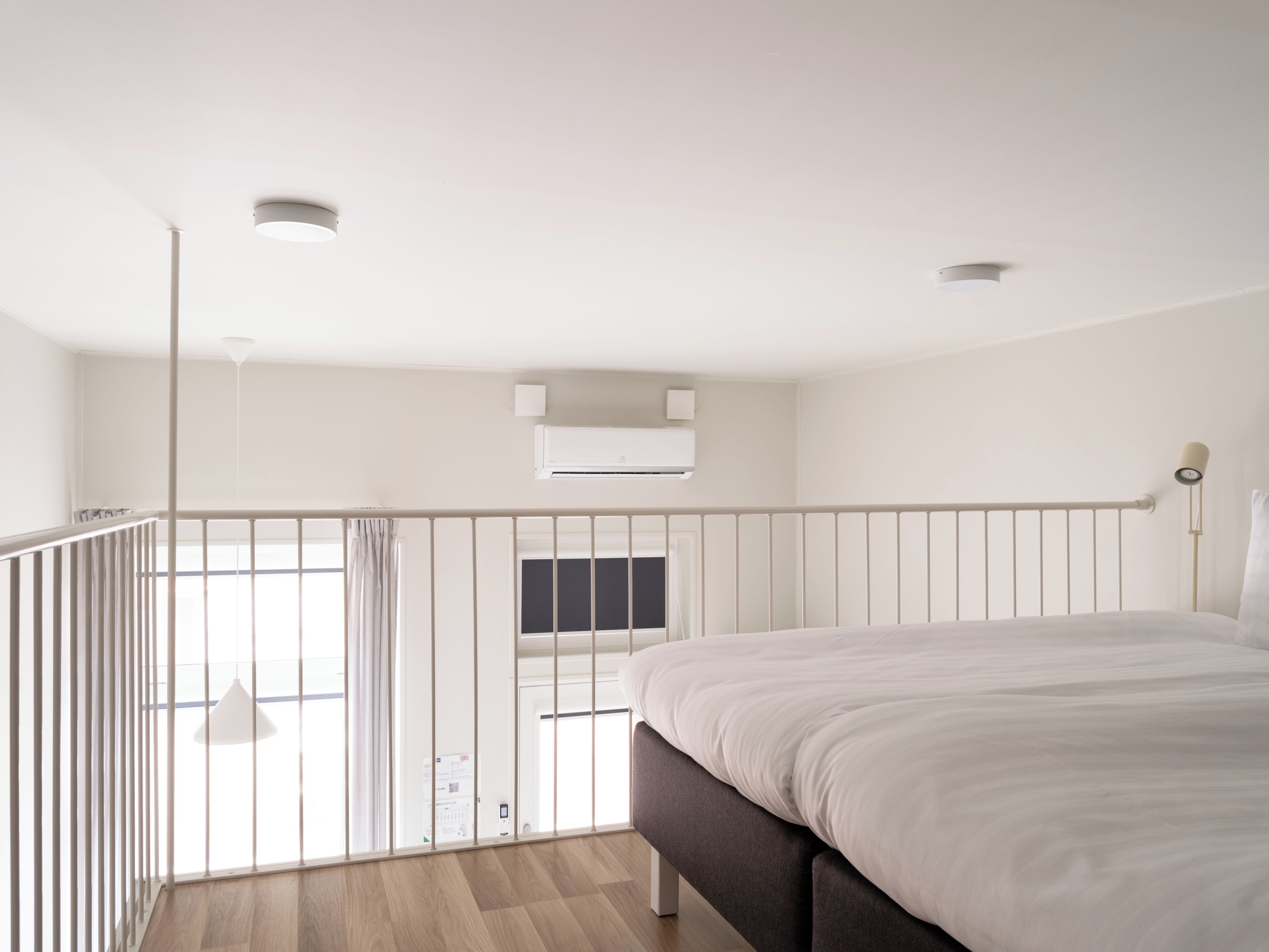 A modern bedroom with a large bed, a balcony with a railing, and an air conditioning unit on the wall.