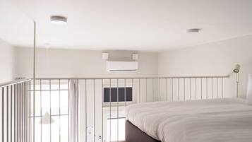 A modern bedroom with a large bed, a balcony with a railing, and an air conditioning unit on the wall.